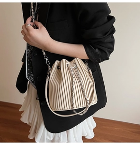 Detail of beige pleated drawstring bucket bag featuring a chain strap on model
