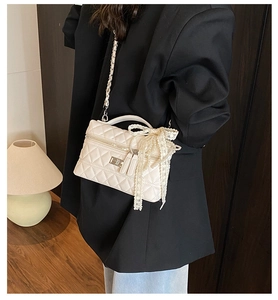 Close-up of white quilted crossbody bag with pearl bow decoration on a black blazer