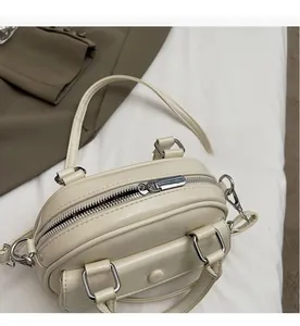 Detail view of smooth silver metal zipper on cream white bowling handbag with leather texture