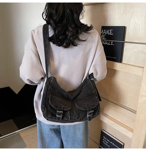 Detail of dark grey washed denim biker bag featuring two front utility pockets and wide strap