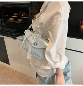 Détail du sac à main en cuir verni bleu clair avec nœud en dentelle et perles