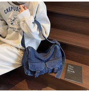 Detail view of denim crossbody bag with dual buckled pockets on wood steps