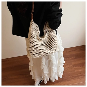 Detailed shot of an off-white crochet tote bag with dark brown leather straps on a model