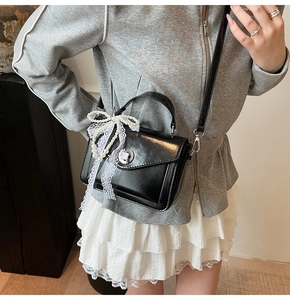 Détail du sac bandoulière noir avec nœud en dentelle blanche et perles sur l'anse