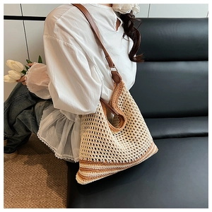 Detail of hand-woven straw shoulder bag with striped base and brown leather strap