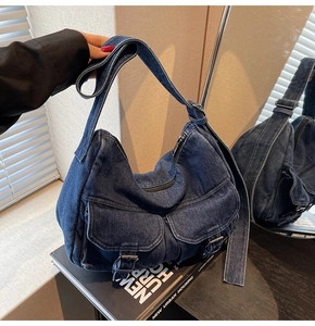 Detail view of denim shoulder bag featuring silver zippers and front buckle pockets