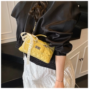 Detail of yellow quilted crossbody bag with lace bow and gold chain strap on model