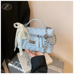 Detail of light blue quilted handbag featuring metal chain and white lace bow with pearls