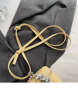Detail of yellow lychee leather crossbody bag with silver heart charm and slim strap
