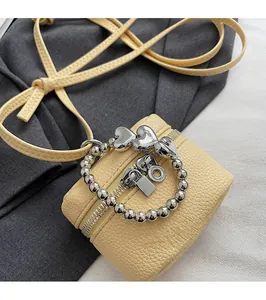 Detail of light yellow lychee grain leather mini bag with silver heart chain accessory