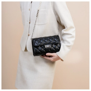 Détail d'un sac bandoulière matelassé noir avec chaîne en perles sur tenue crème