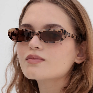 Vintage tortoiseshell oval sunglasses with dark brown lenses worn by a fashion model