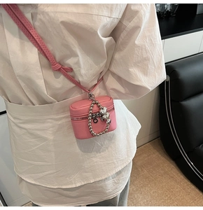 Detail view of pink leather mini bucket bag with silver letter pendants and cross-body strap