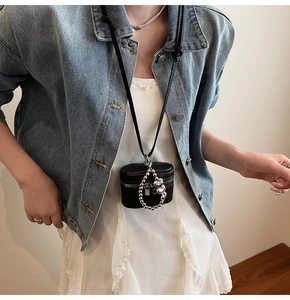 Detail of a mini black leather cylindrical neck bag with silver charms and chain