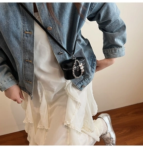 Detail of mini black leather crossbody bag with silver heart chain on a blue denim jacket