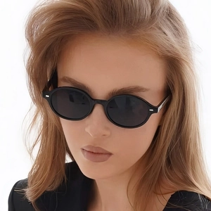 Retro minimalist oval sunglasses in black frame worn by a model against white background