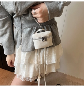 Detailed macro view of white pebble-grain mini bag with silver zipper and beaded chain