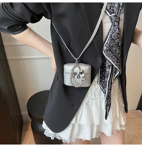 Detail of silver mini crossbody bag with heart pendant on model's black suit