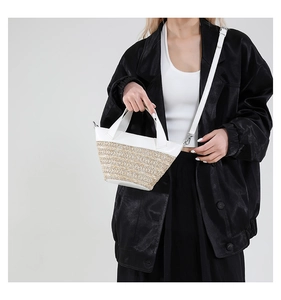 Detail of hand-woven straw and white leather patchwork bucket bag with crossbody strap