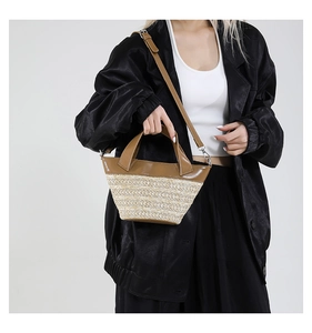 Detail of woven straw bucket bag with brown leather handles and adjustable shoulder strap