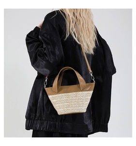 Detail view of woven straw bucket bag with brown leather handles on a model in black dress