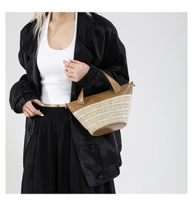 Detailed view of woven straw bucket bag with brown leather trim and metallic rings