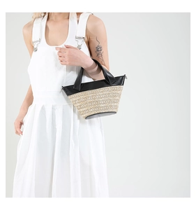 Detail of woven straw bucket bag with black leather trim held by a model in white