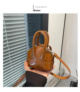 Détail d'un mini sac bandoulière en cuir verni marron avec poignées et zip argenté