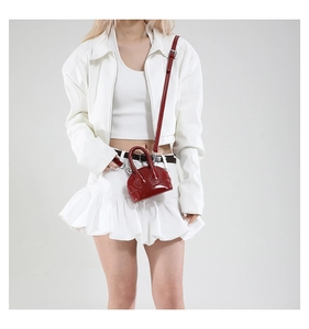 Détail d'un mini sac à bandoulière rouge foncé en cuir verni sur un mannequin