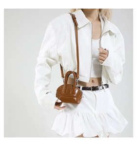 Détail d'un mini sac coquille en cuir verni marron porté par un mannequin avec bandoulière