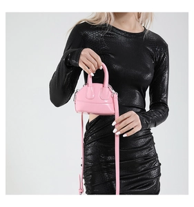 Mini sac bandoulière en cuir verni rose porté par un mannequin en robe imprimé serpent