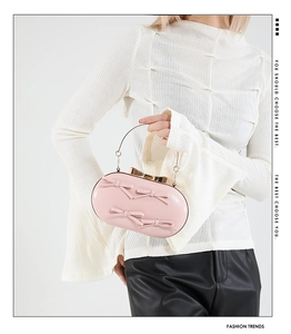 Detail of pink oval evening clutch with 3D bows and golden metal handle on model