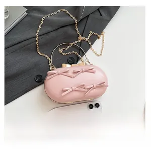 Pink bow evening clutch bag with gold chain and phone size comparison on table
