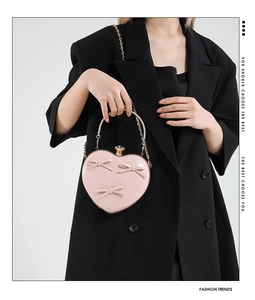 Detailed shot of pink heart-shaped bag with 3D bows and metal handle held by a model