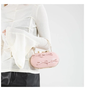 Detail of pink oval hard-shell clutch bag with decorative bows and gold metal frame