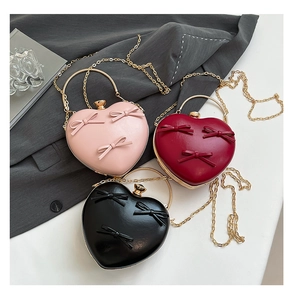 Three heart-shaped evening bags in pink, red, and black with bow accents and gold chain