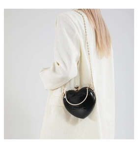 Model wearing black heart-shaped clutch with bow details and gold chain strap