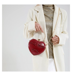 Detail of red heart-shaped evening bag with bow accents and gold metal top handle