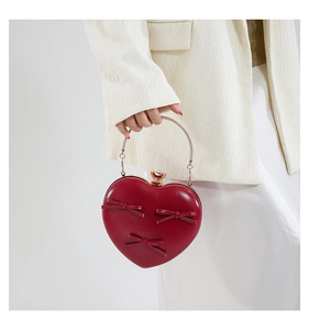 Detail of red heart evening clutch featuring silk bows and a metal handle held by model