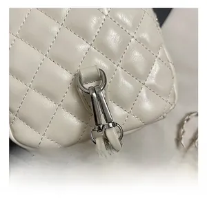 Macro detail of silver D-ring and leather-threaded chain on quilted cream white bag