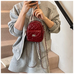 Detail of burgundy quilted patent leather backpack with silver twist lock and chain strap