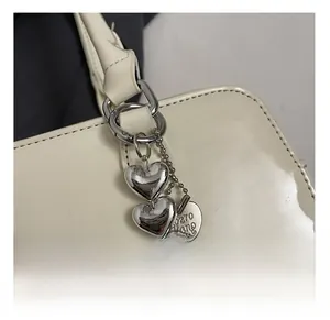 Détail d'un pendentif triple cœur métallique avec logo sur sac en cuir verni crème
