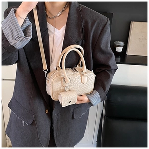 Detail of beige woven texture bowling bag with mini charm pouch on a shoulder strap