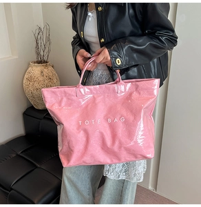 Dettaglio di una borsa tote rosa lucida con scritta TOTE BAG bianca e modella