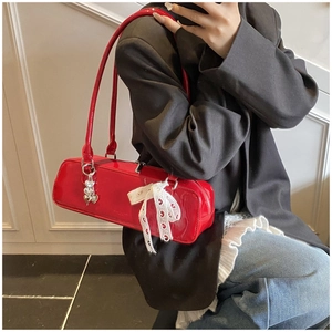Détail d'un sac sous le bras en cuir verni rouge avec nœud en dentelle et pendentif cœur