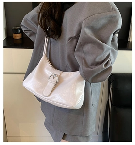 Detailed close-up of white glossy leather underarm bag with silver round buckle decoration