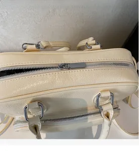 Close-up of smooth silver dual metal zippers on a cream faux leather Boston bag