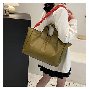 Olive green tote bag with a contrasting red ruffled shoulder strap worn by a model