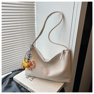 Detailed texture of beige lychee grain leather tote bag with elephant charm on book
