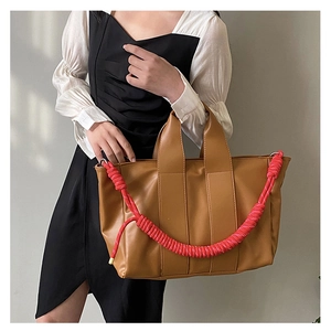 Detail of a brown PU leather tote bag featuring a vibrant red braided rope handle